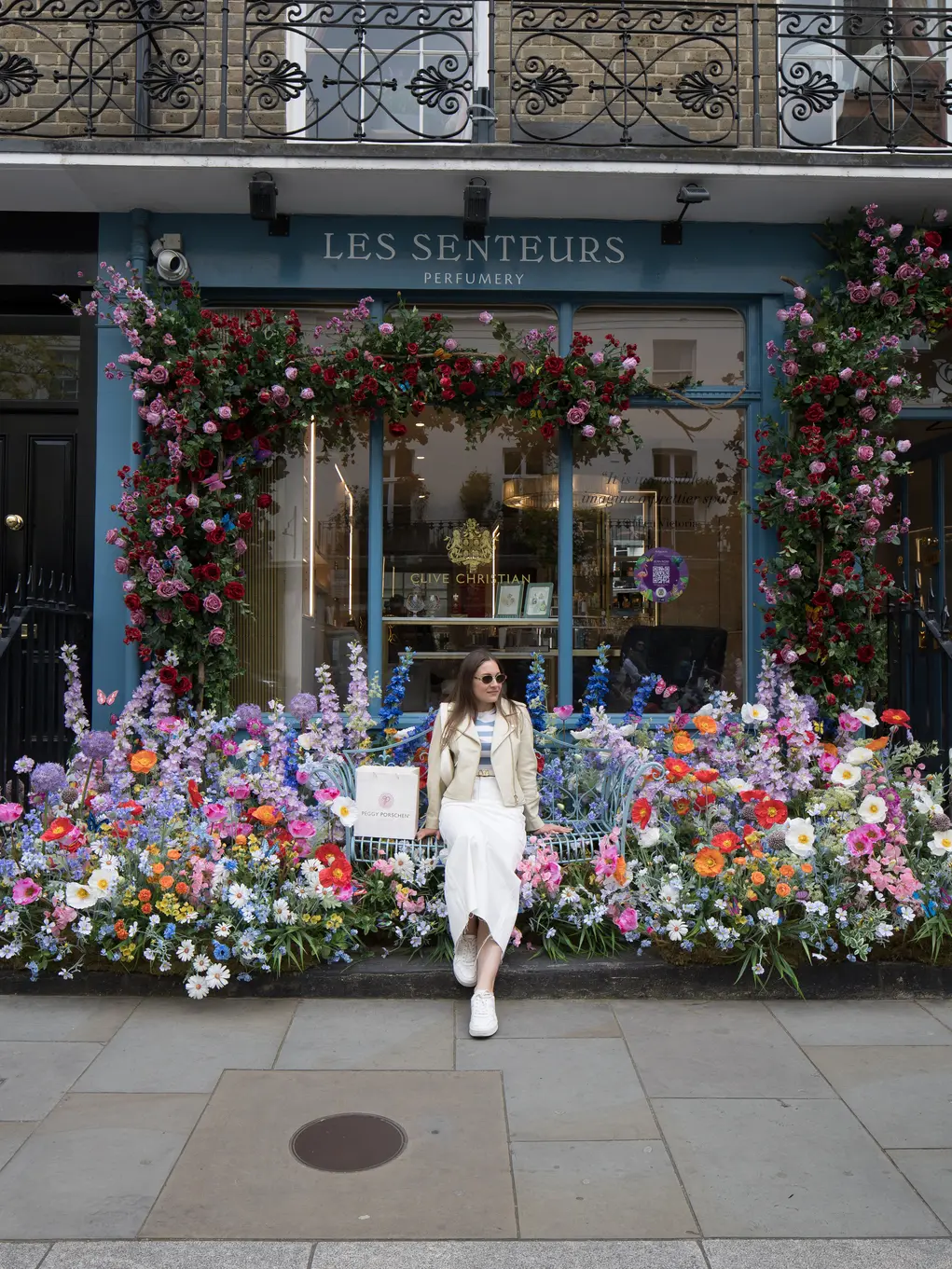 A girl poses outside a shop covered in a huge floral display