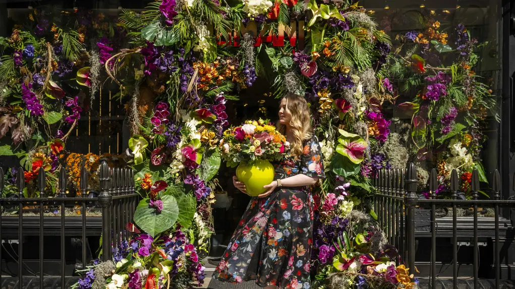 A woman in a floral dress stands outside the Neill Strain Floral Couture shop with its floral display