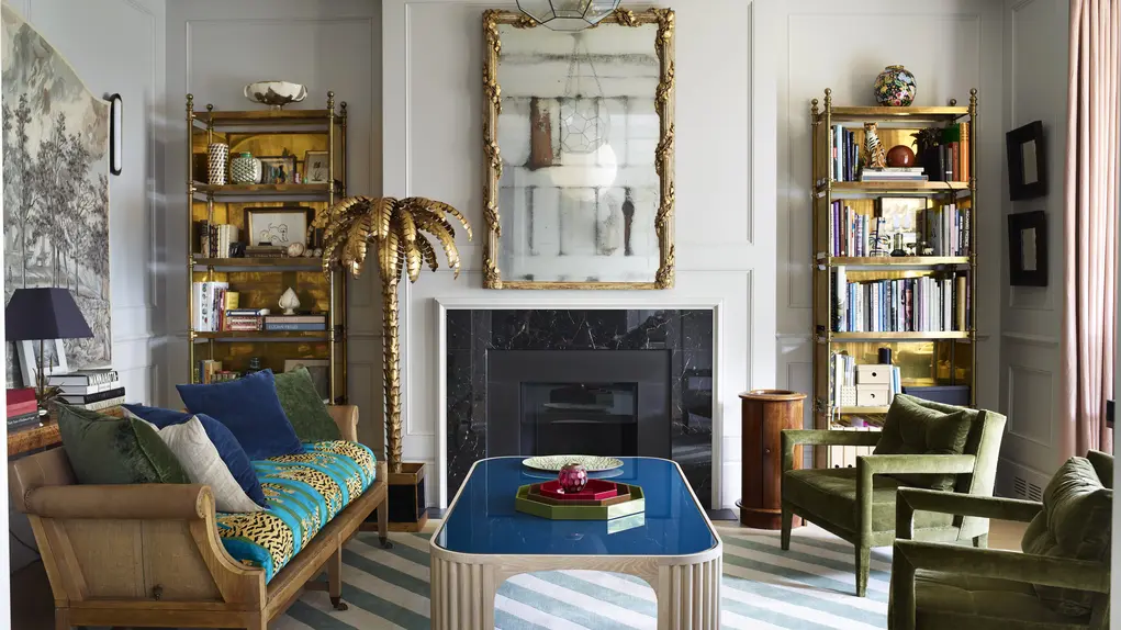 A living room with a blue lacquered table, two chairs and a fireplace with a mirror 