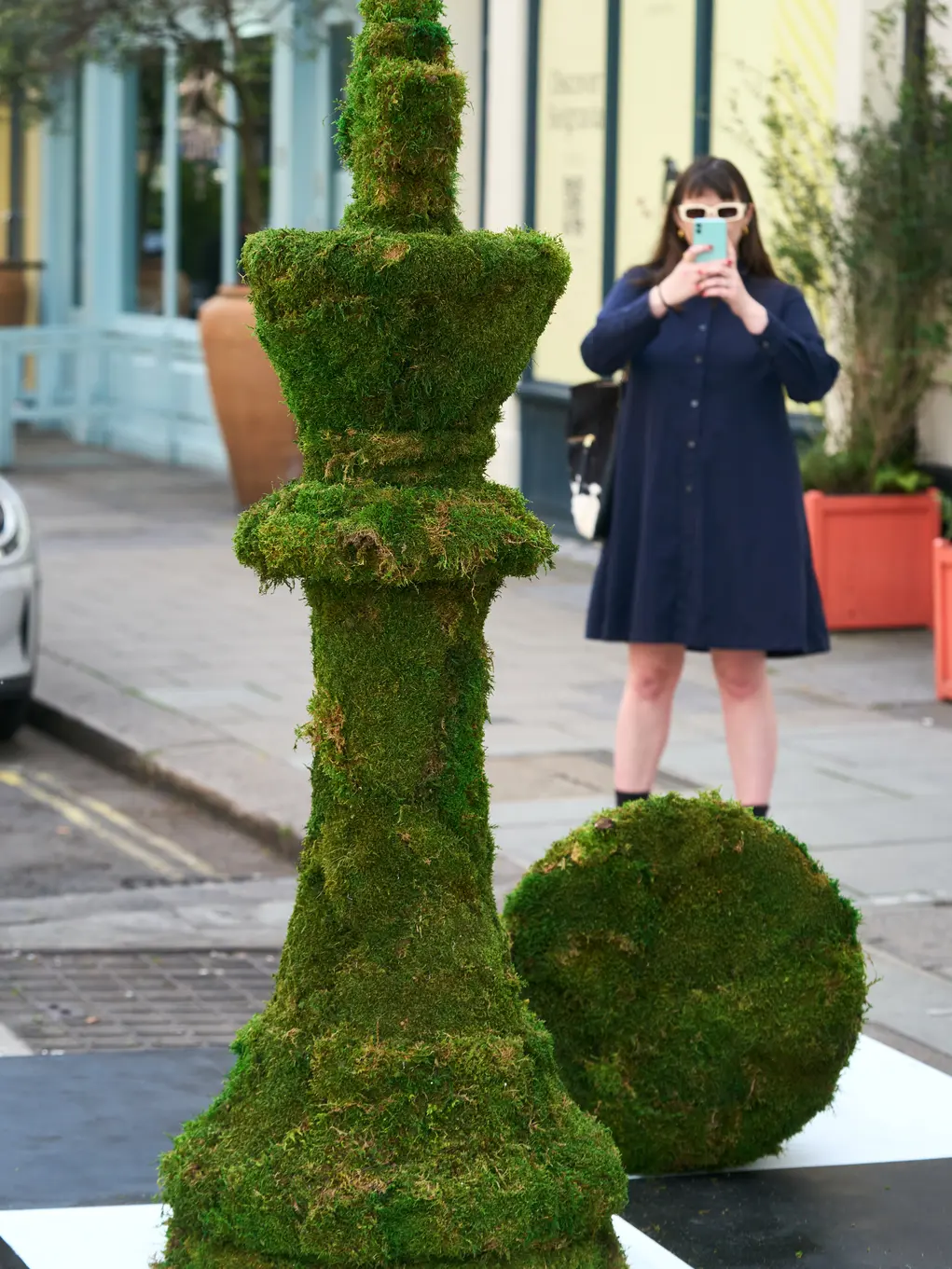 A woman takes a photos of a chess piece made of plants