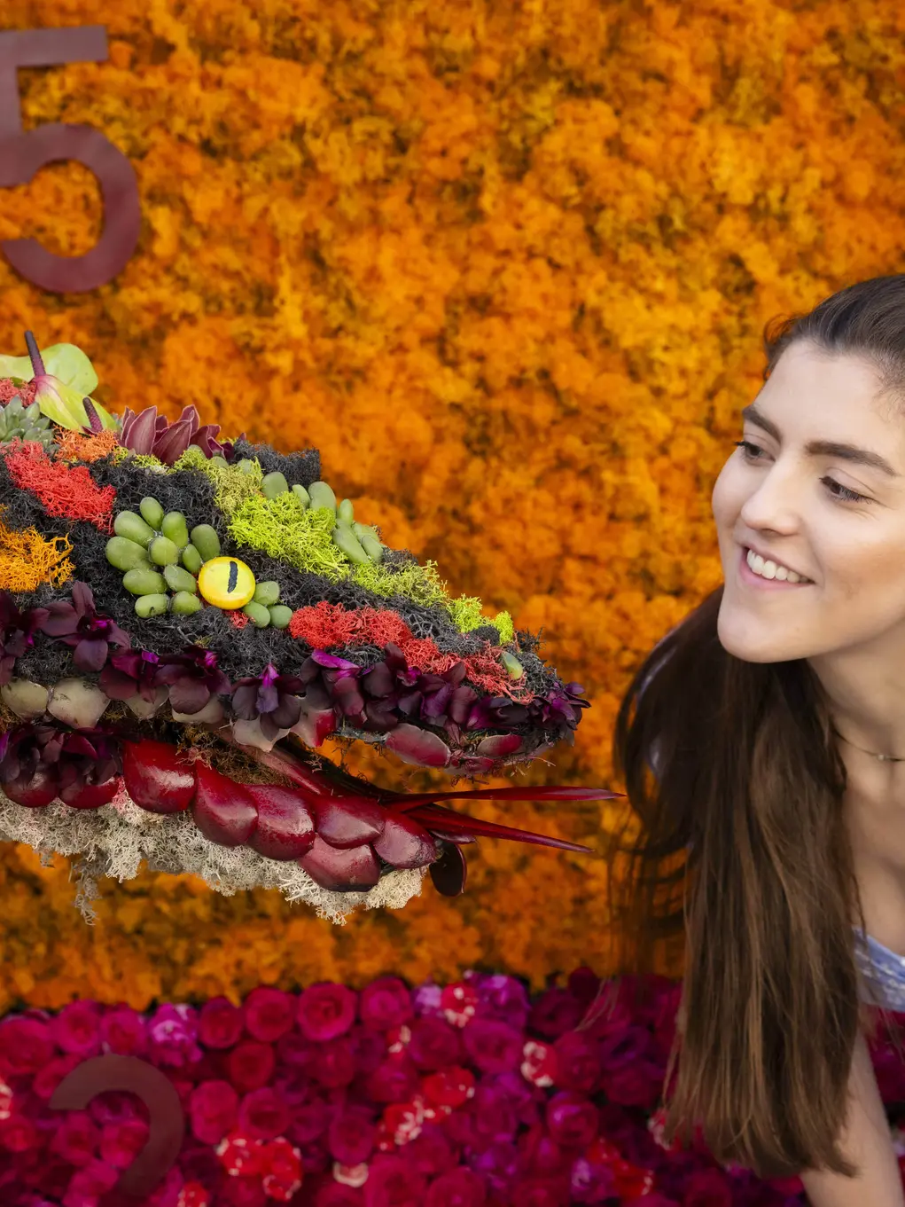 A girl in a blue dress looks at the snake floral display