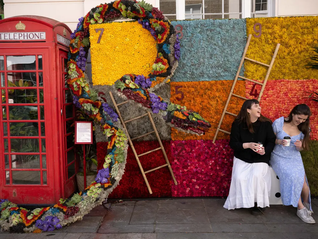 A snakes and ladder floral display next to a phone box with two women laughing