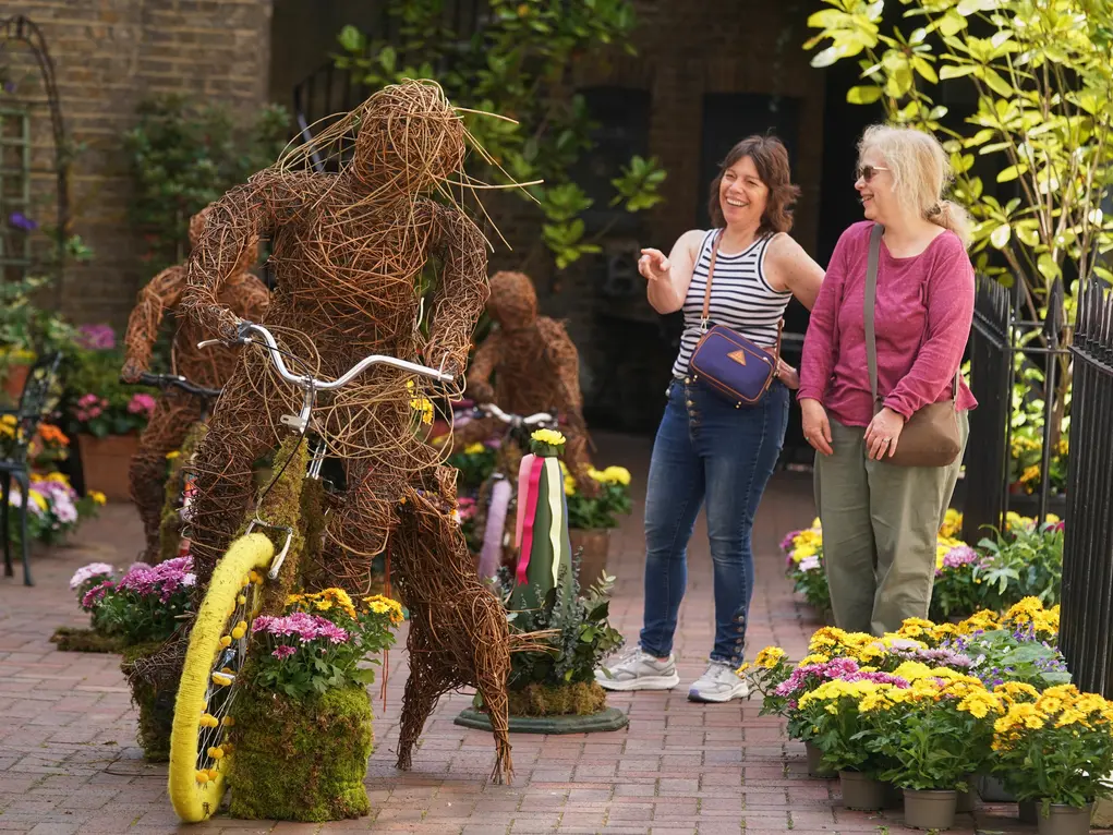 A plant display of a person riding a bicycle while two people look on
