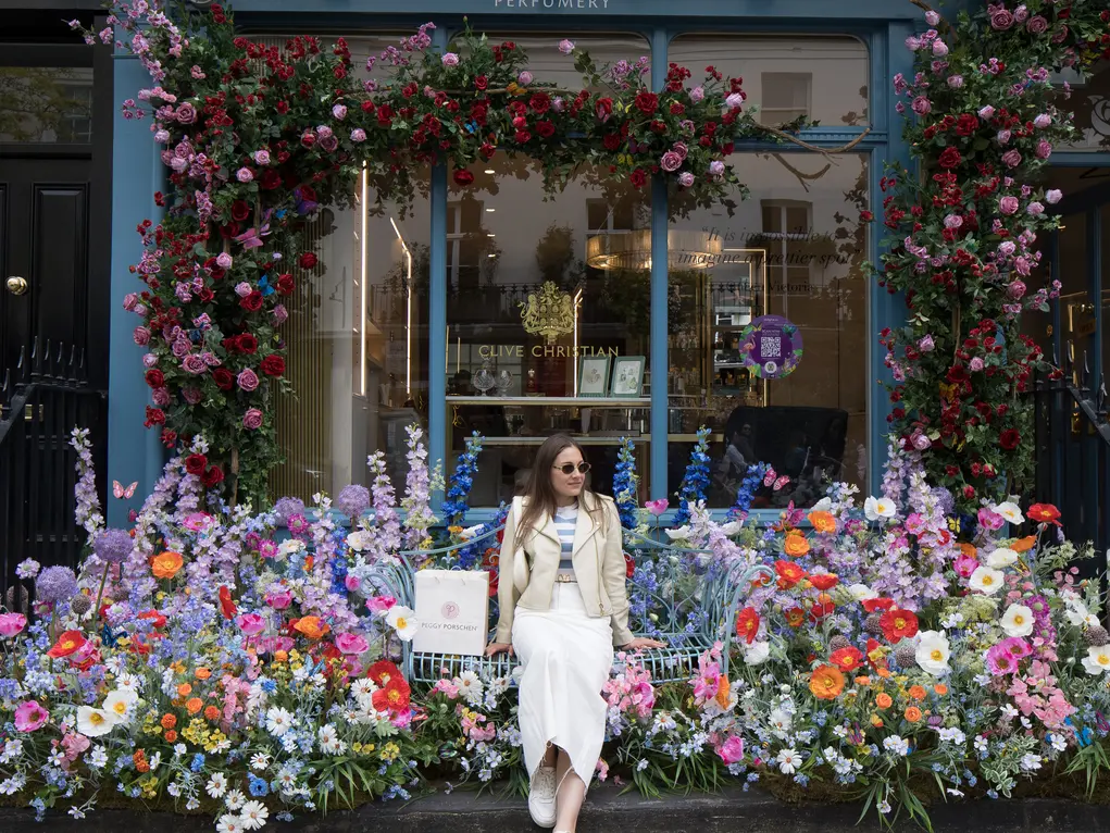 A girl poses outside a shop covered in a huge floral display