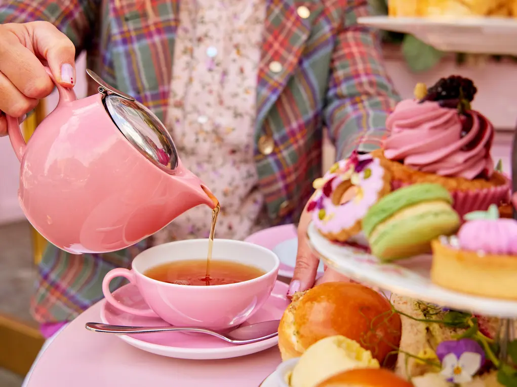 A hand pouring a cup of tea with a pink teapot
