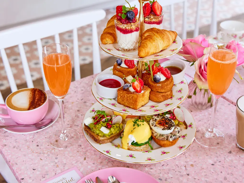 Afternoon tea showing cakes on a tiered cake tray with flutes of an orange drink