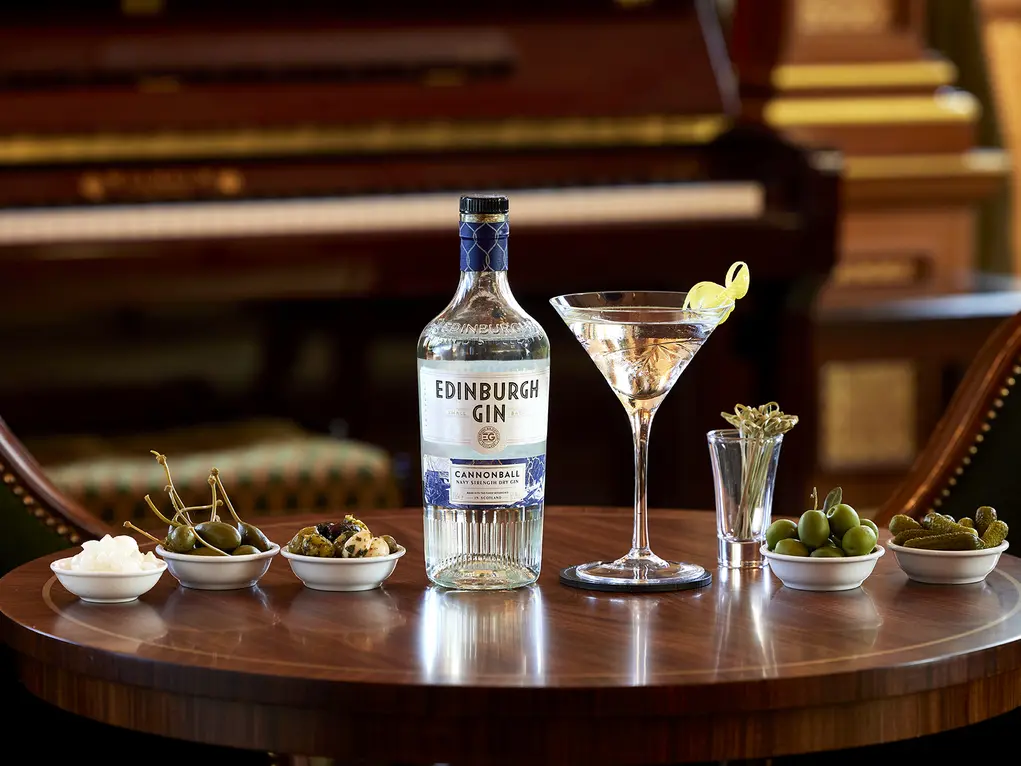 A circular table with a Martini cocktail and a bottle of gin with small bowls of olives