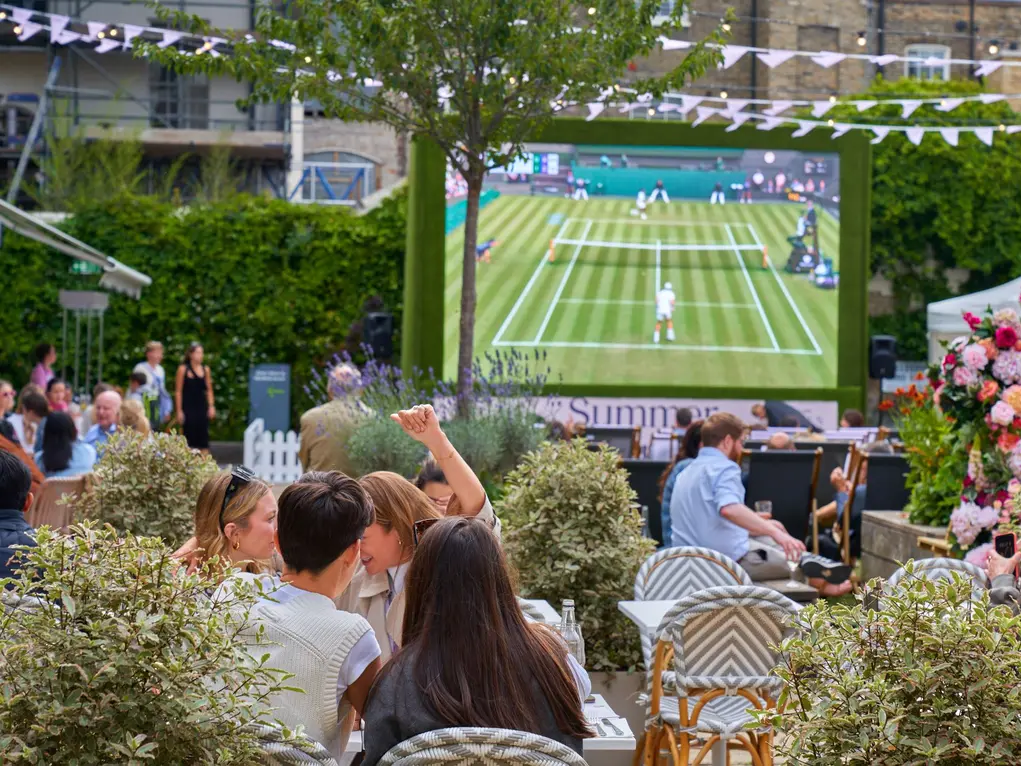 A crowd of people watch Wimbledon on a big screen